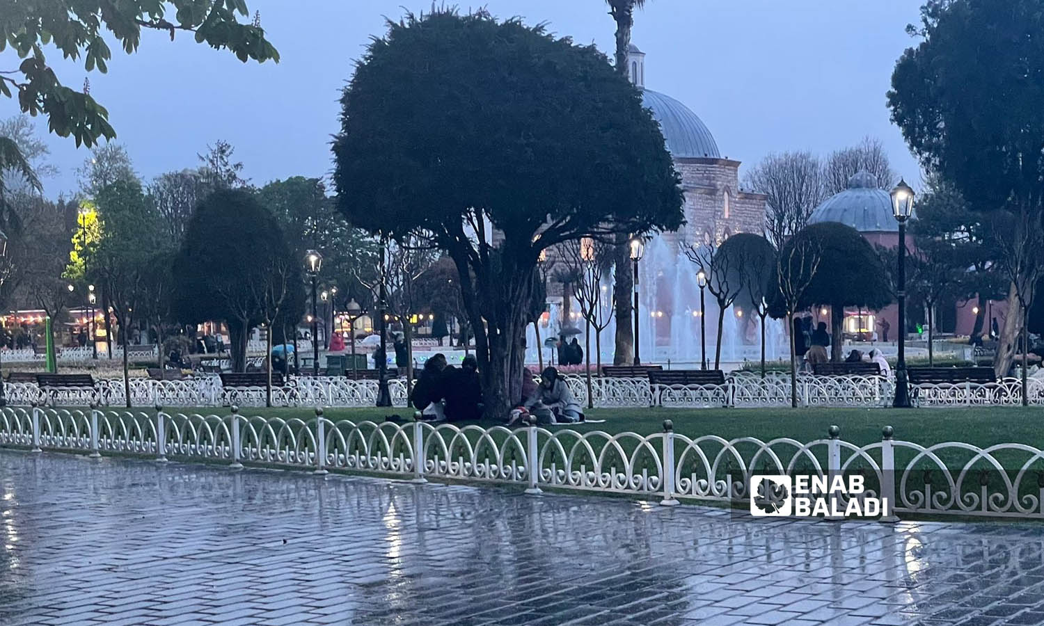 عائلة سورية تجلس تحت أغصان شجرة تفاديًا للمطر خلال انتظارها وقت الإفطار- 18 نيسان 2023 ()