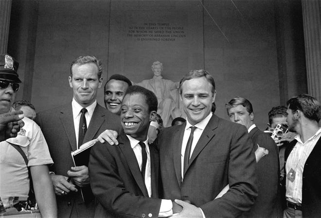 Actor Marlon Brando, right, poses with his arm around James Baldwin, author and civil rights leader, in front of the Lincoln statue at the Lincoln Memorial, August 28, 1963, during the March on Washington demonstration ceremonies which followed the mass parade. Posing with them are actors Charlton Heston, left, and Harry Belafonte.