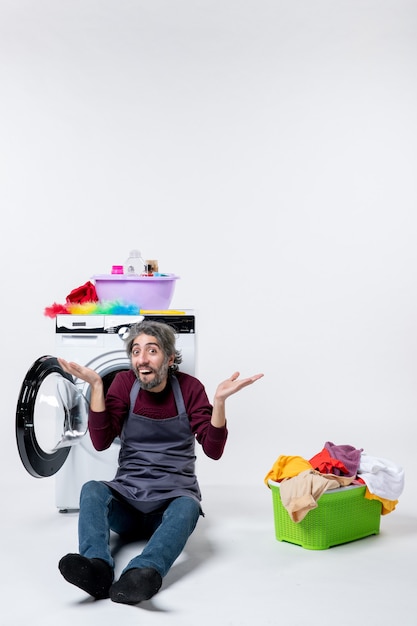 Free photo front view surprised male housekeeper sitting in front of washer laundry basket on white wall